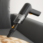 Black cordless handheld vacuum with a clear dust cup pictured beside a sofa.